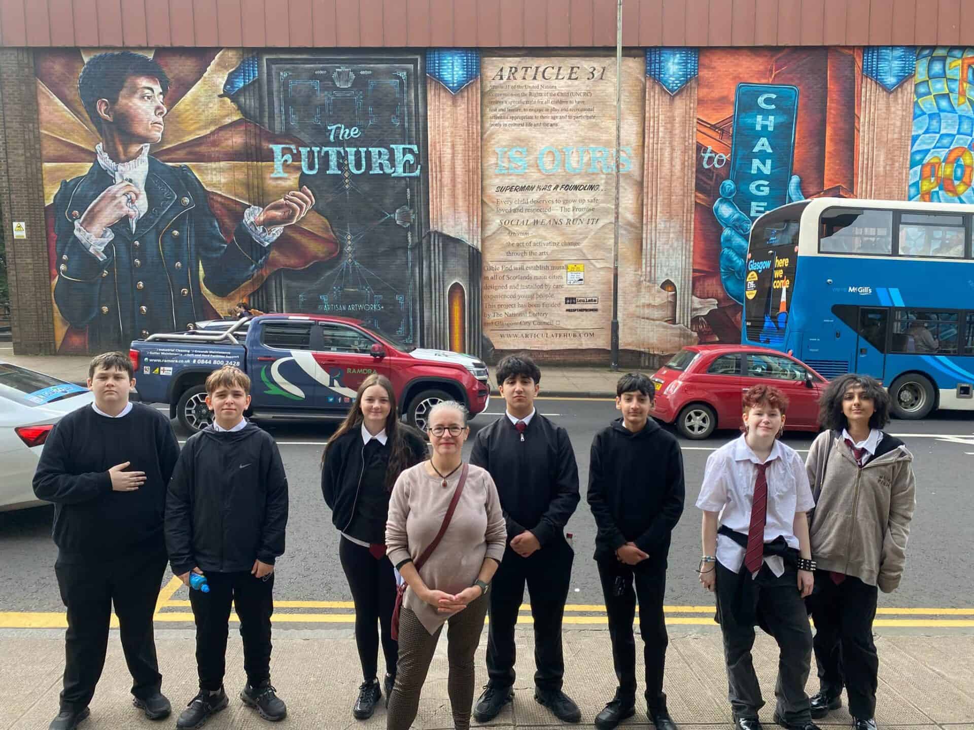 Group of young people and adults in front of a mural about the BSL Act 2015 in Scotland.