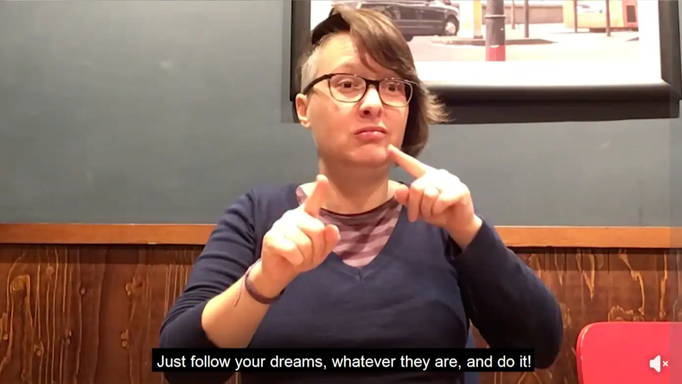 Deaf woman using sign language in a cafe, promoting BSL awareness.